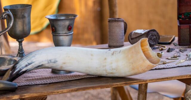 An animal drinking horn and silver cups on a table top.