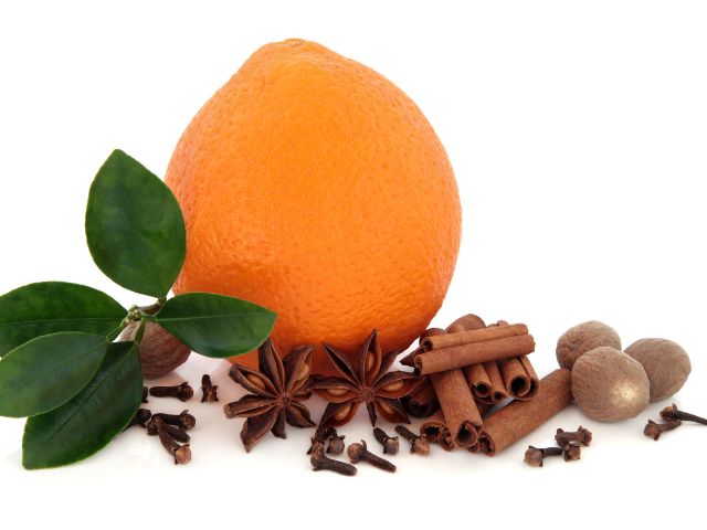 An orange fruit and different spices such as nutmeg, star anise, and more.