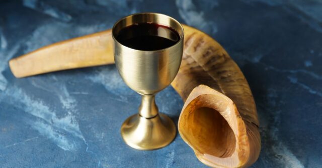 A gold goblet containing wine with an animal horn beside it.