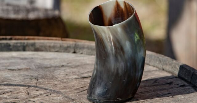 A drinking tankard made out of animal horn in a wooden table.