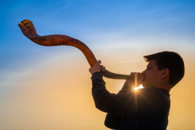 A boy trying to use a blow horn in modern day.