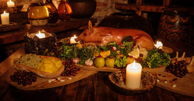 Ancient style dinner setting with a whole roasting pit and various fruits, vegetable and nibbles laid out.